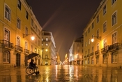 Man in a wheelchair in an empty wet city pedestrianised street.