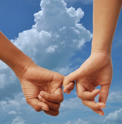 a male and female hand with little fingers entwined with blue sky background.